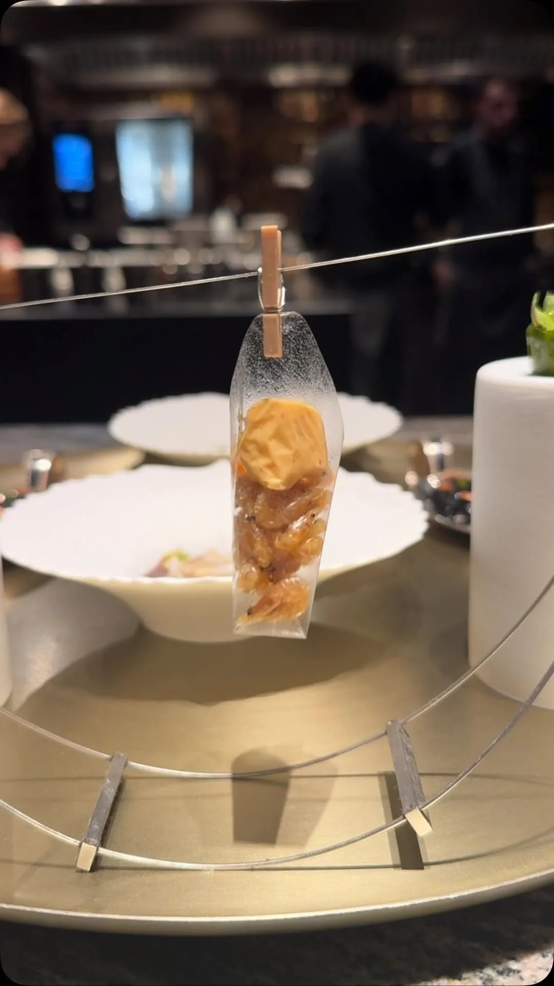 A small tasting bite in a glass cone suspended over a white bowl on a metal stand