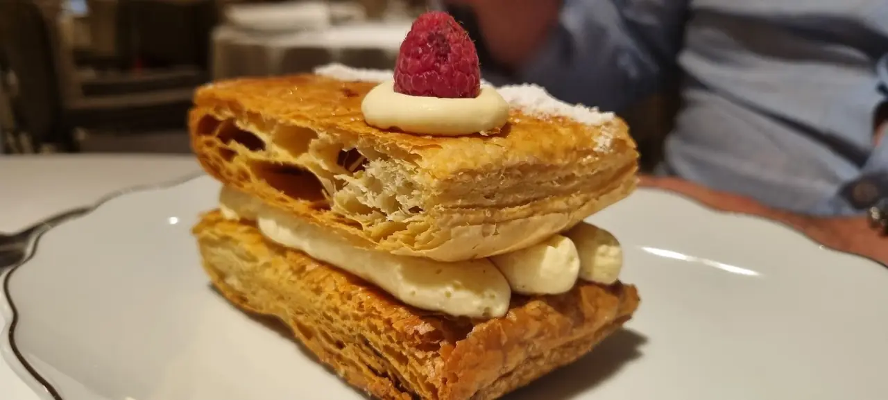Mille-feuille pastry with piped cream filling, topped with a raspberry and powdered sugar