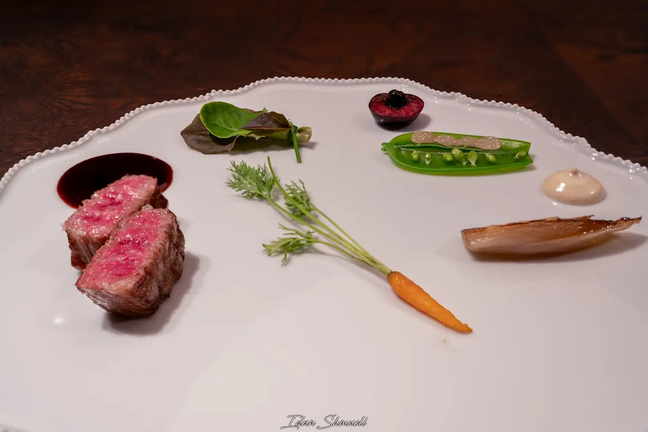 Sliced rare beef with red wine sauce, plated alongside baby carrot, snow pea, cherry, shallot and a cream dollop