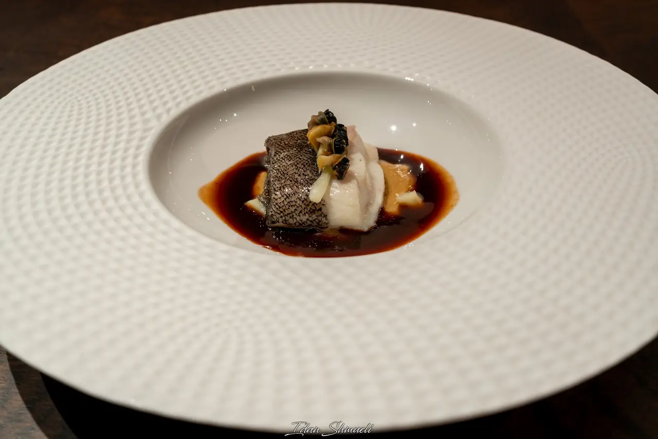 Seared fish fillet with crispy skin, mushrooms and a dark reduction sauce on a large white plate
