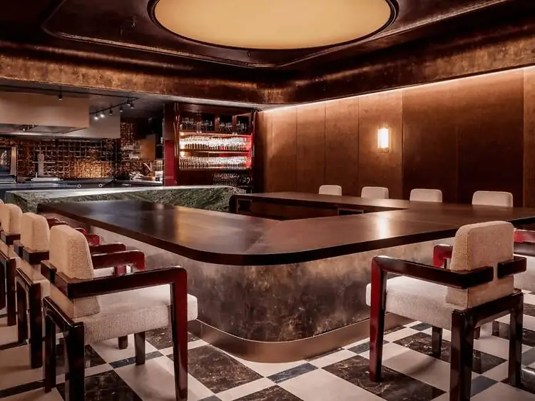 Dining room at Ramón Freixa Atelier, with a long counter, cushioned chairs and a chequered marble floor