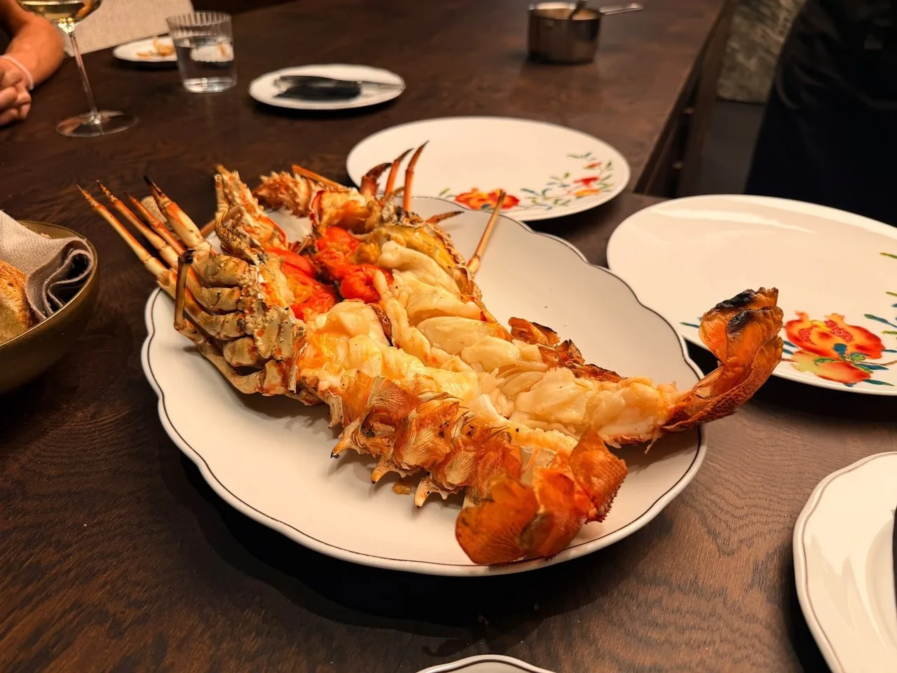A large orange crustacean on a platter on a dark table with small plates around it