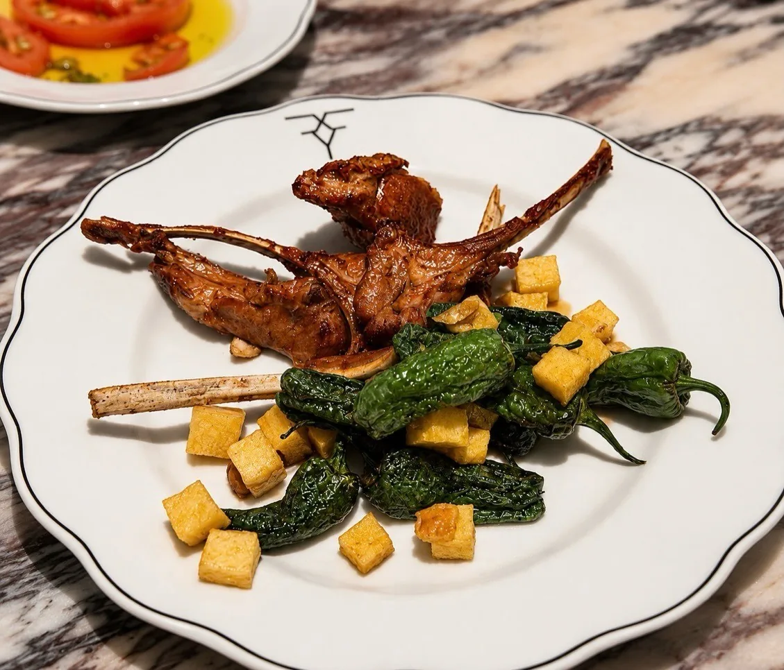 A roasted small bird on a white plate with green peppers and small golden cubes
