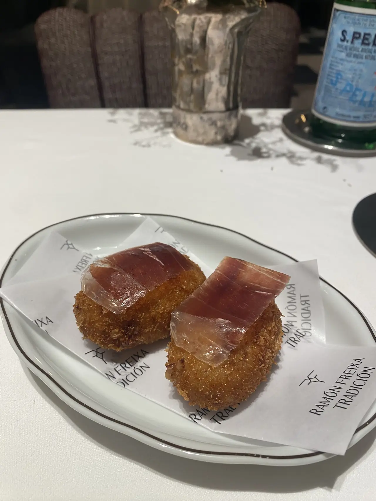 Two breaded croquettes each topped with a slice of cured ham, on branded napkins over a white plate