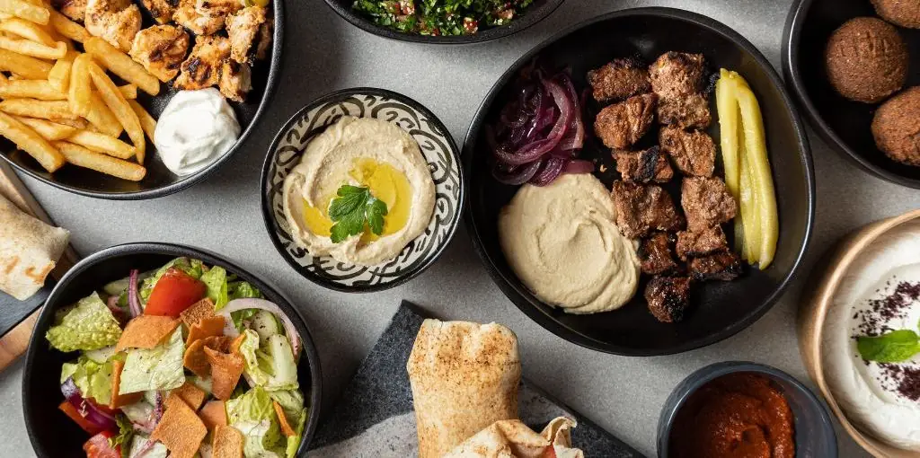 Overhead Middle Eastern spread with hummus, grilled meat skewers, falafel, fattoush salad, fries with garlic sauce and pita