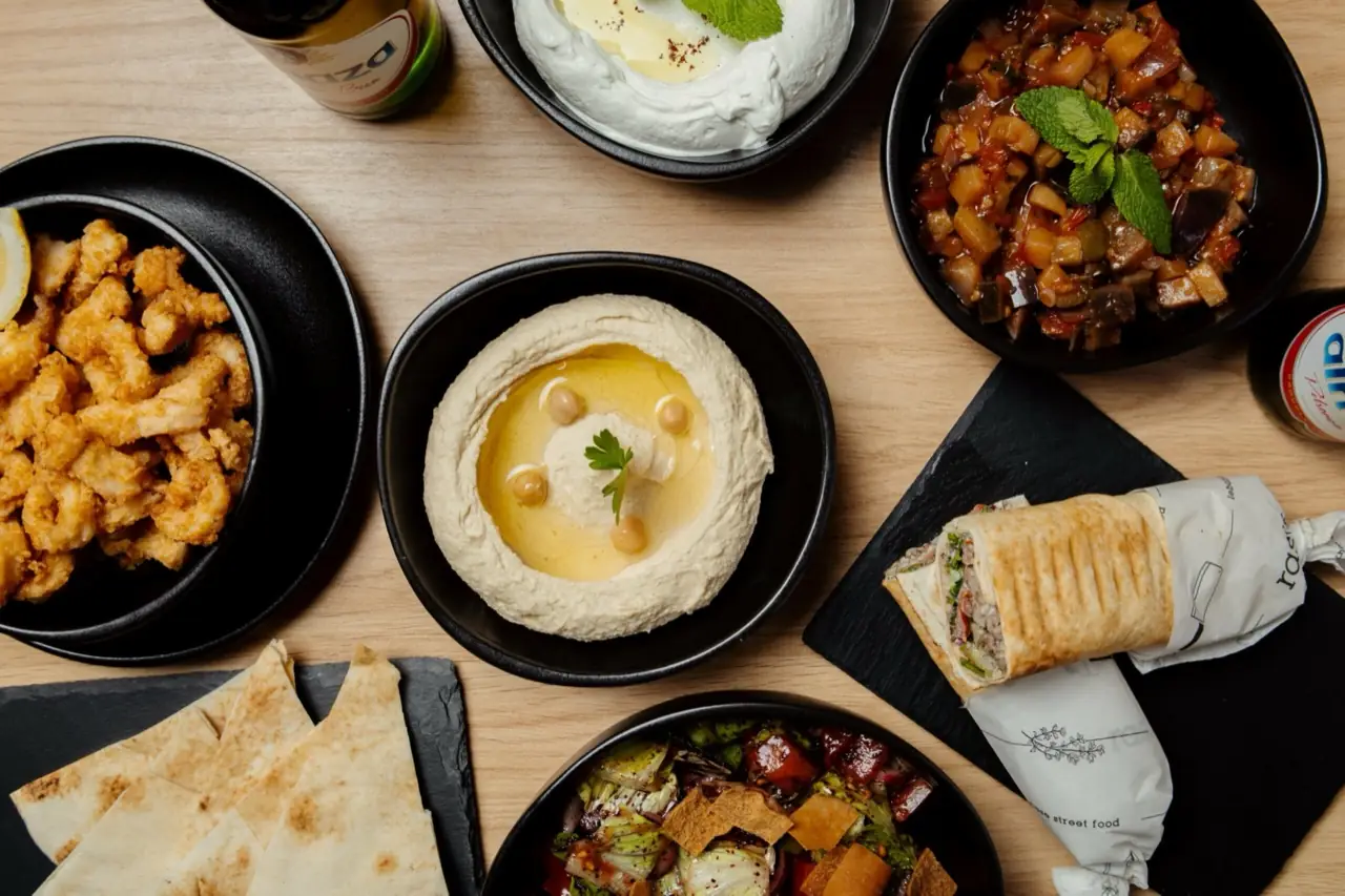 Hummus, fried chicken bites, a wrapped shawarma and Lebanese bread on a wooden table