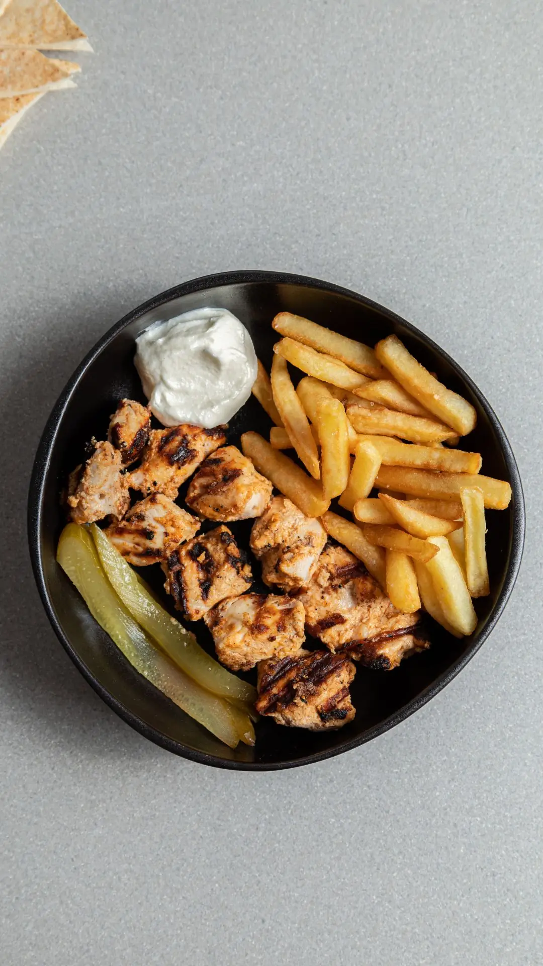Grilled shish taouk chicken with chips, garlic sauce and pickles in a black bowl