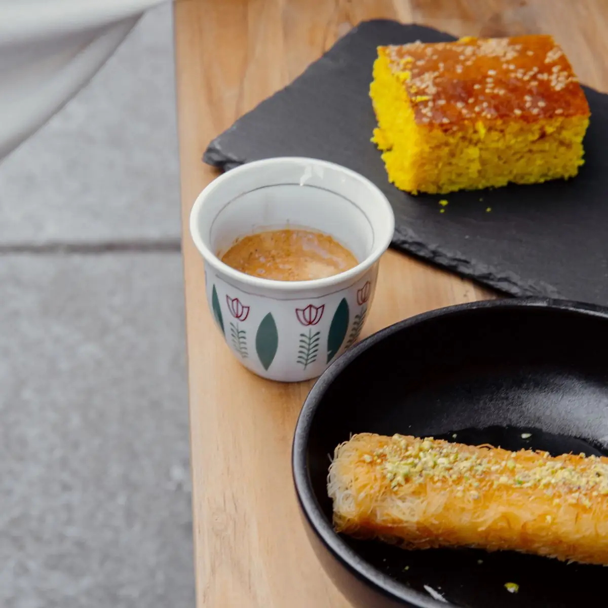 Knefe with pistachio and a cake beside a small cup of coffee