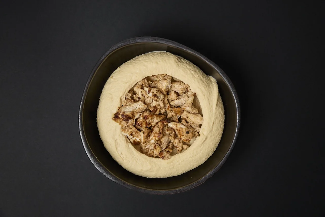 A dark bowl of hummus topped with pieces of grilled chicken