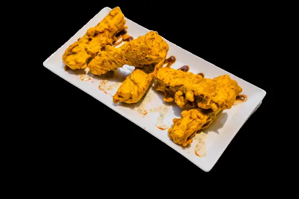 Crispy tandoori chicken strips drizzled with sauce on a white rectangular plate, Rasoi (Rasoi BCN)