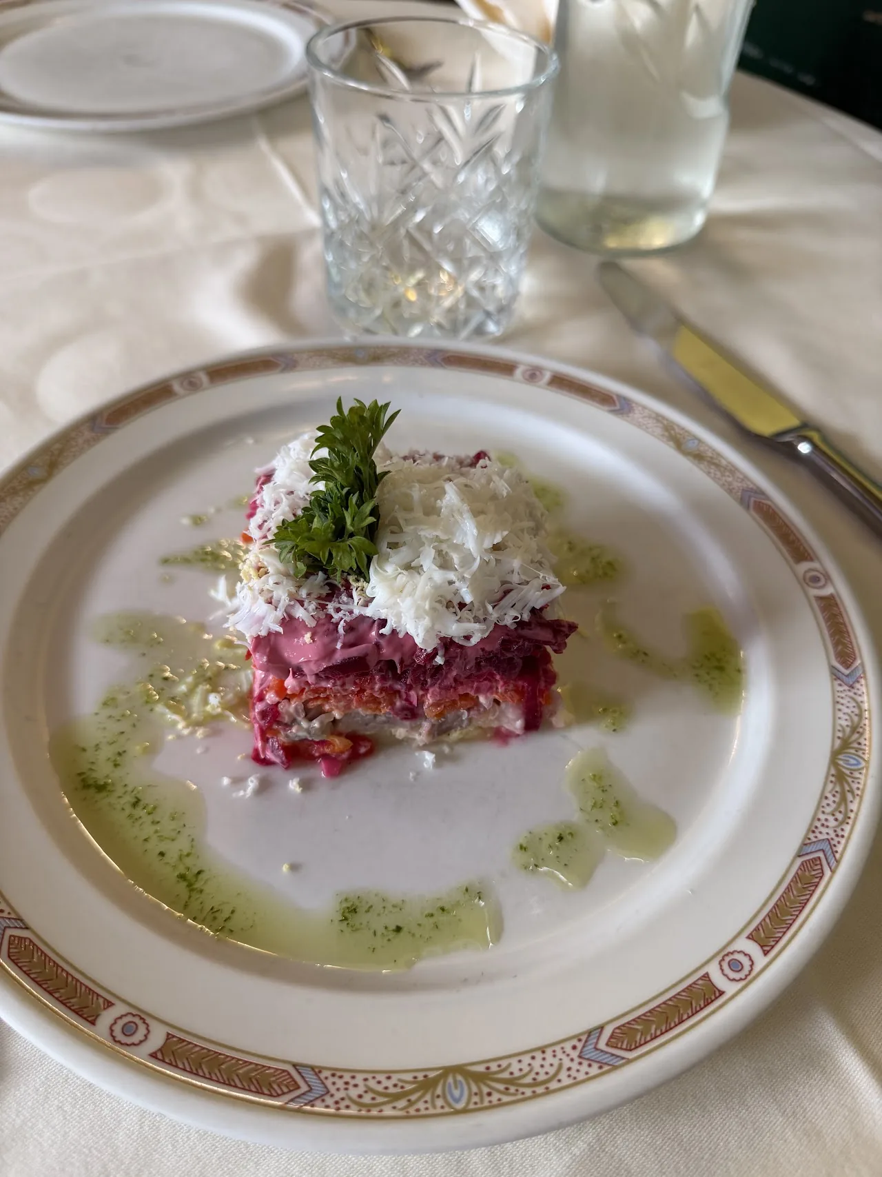 A slice of layered beet and herring salad garnished with a sprig of dill