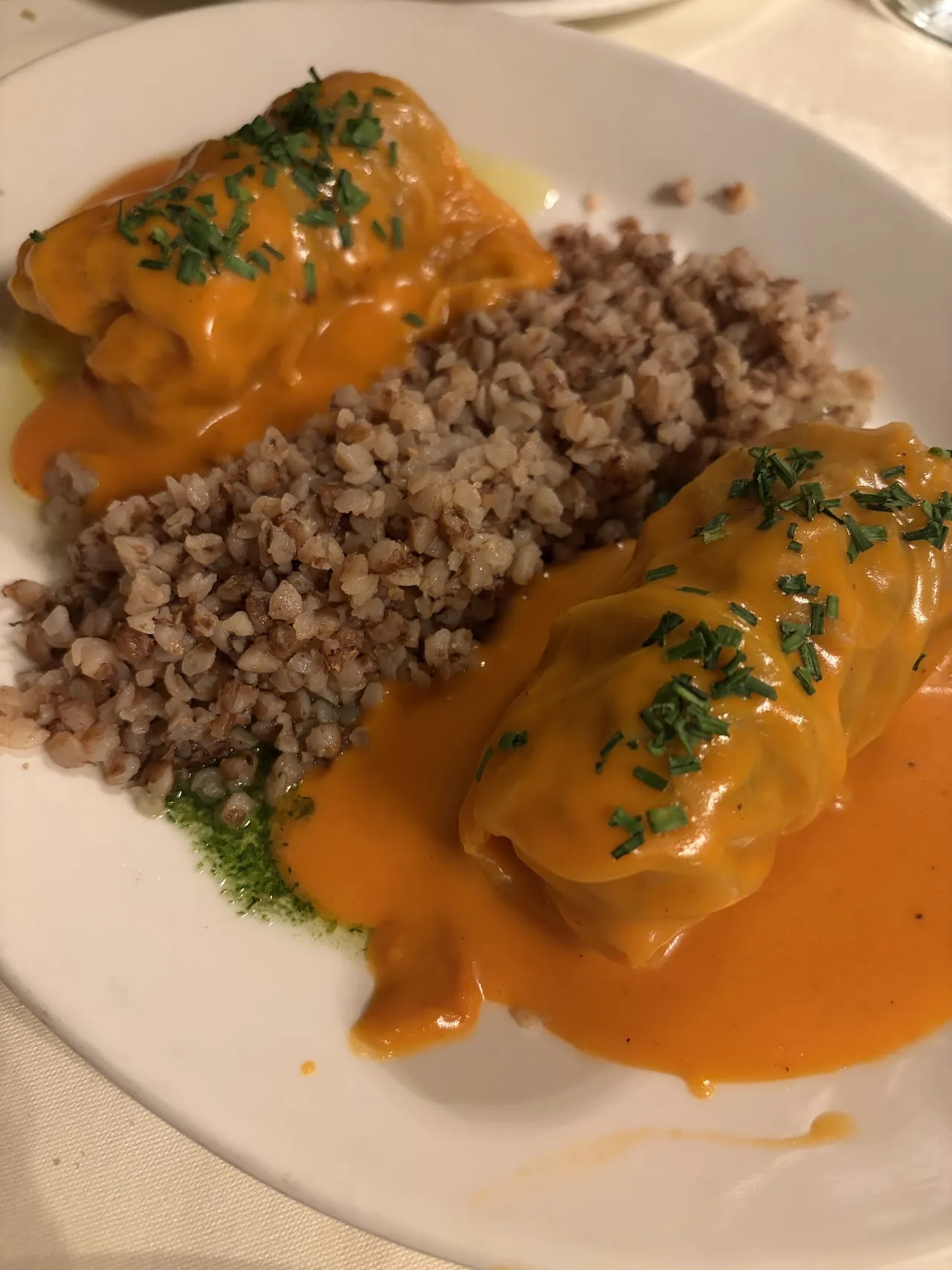 Two stuffed cabbage rolls covered in an orange sauce, served with a side of buckwheat