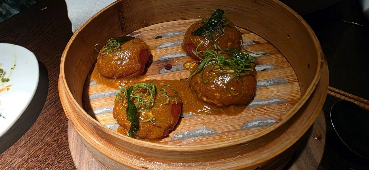 Four glazed dumplings in a bamboo steamer