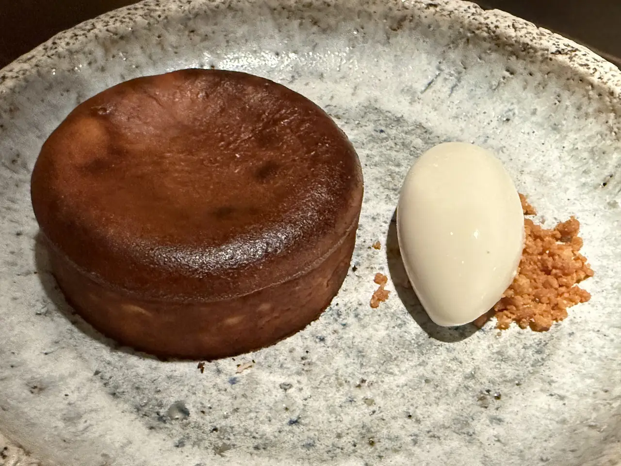 Burnt Basque cheesecake slice beside a quenelle of pale cream and crumble on a speckled plate