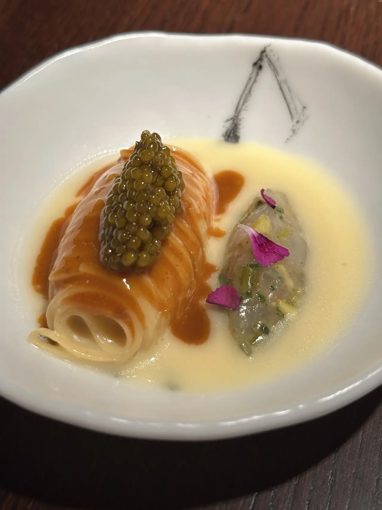 Rolled pasta topped with caviar beside a translucent dumpling with pink petals in a pale broth