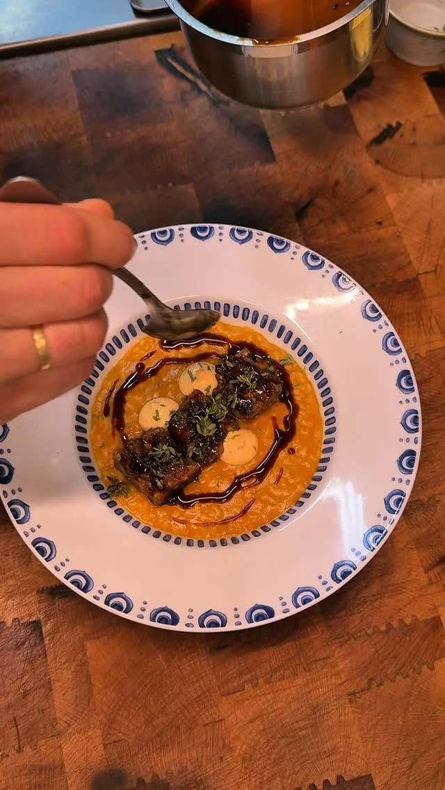 Small plate of a dark sauce dish garnished with herbs, held with a fork