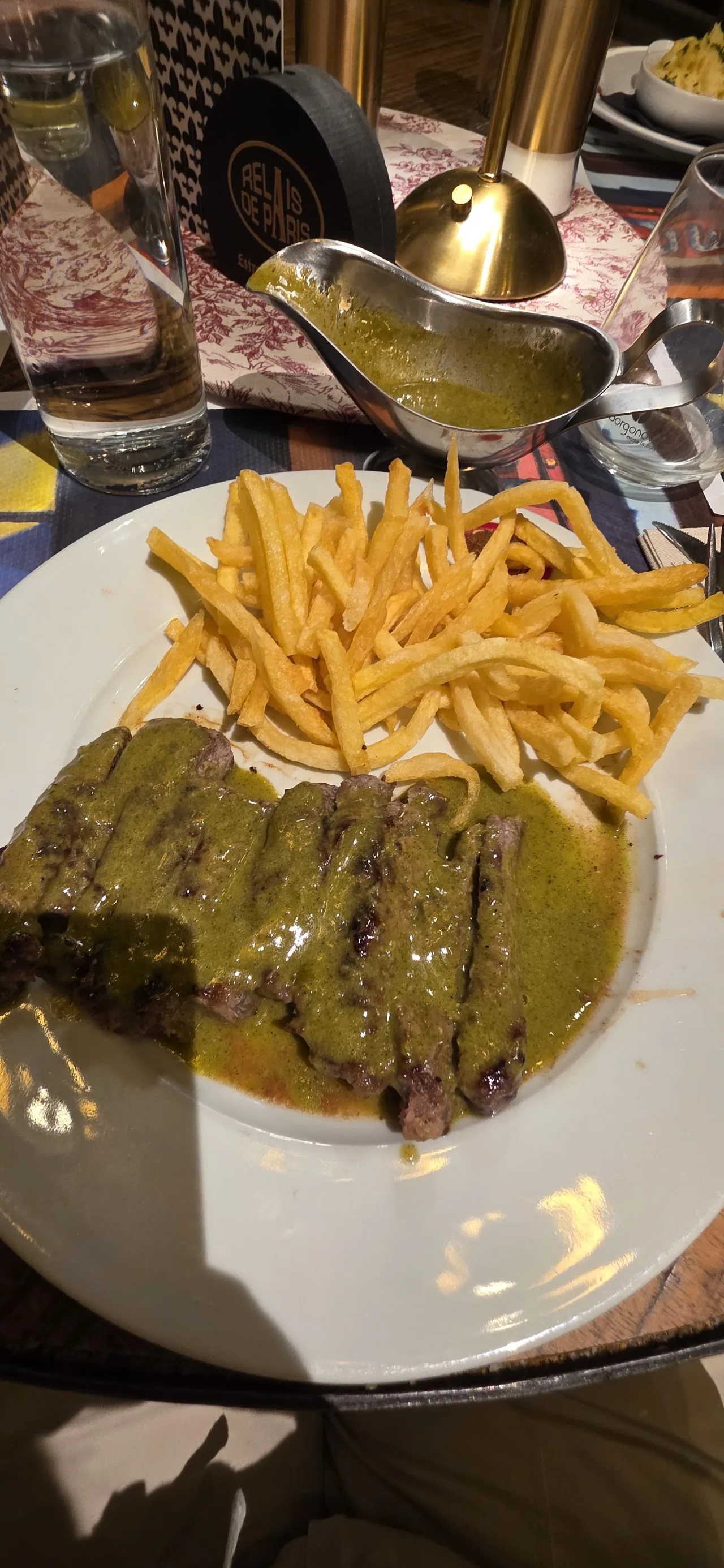 A sliced steak with a green herb sauce, served with a pile of french fries