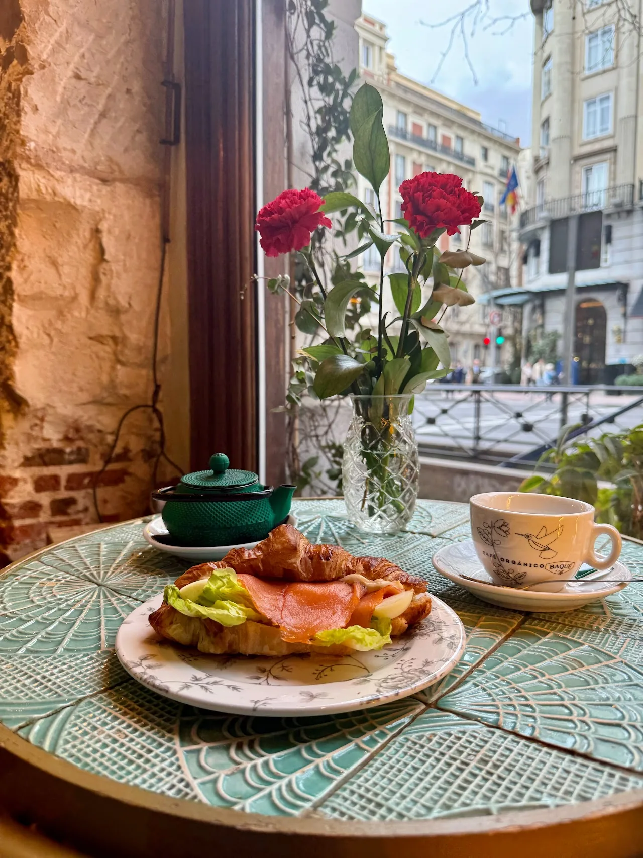 A plate of open-faced toast with a cup of tea and a small teapot on an outdoor café table