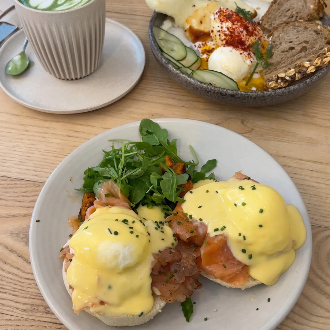 Overhead shot of a smoothie, eggs Benedict, and a granola bowl on a wooden table