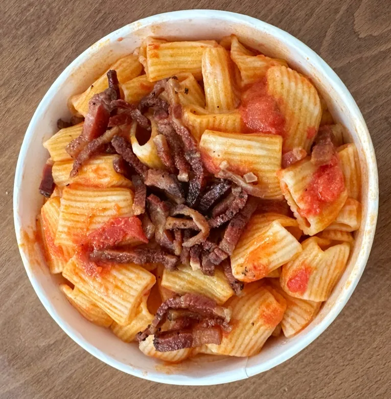 A bowl of rigatoni pasta in tomato sauce with crispy guanciale