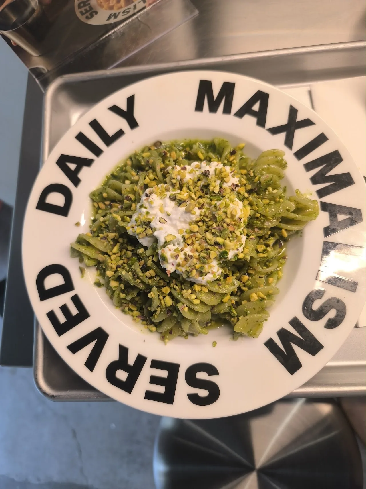 A plate of green pesto pasta with a dollop of ricotta, on a plate with a decorative rim