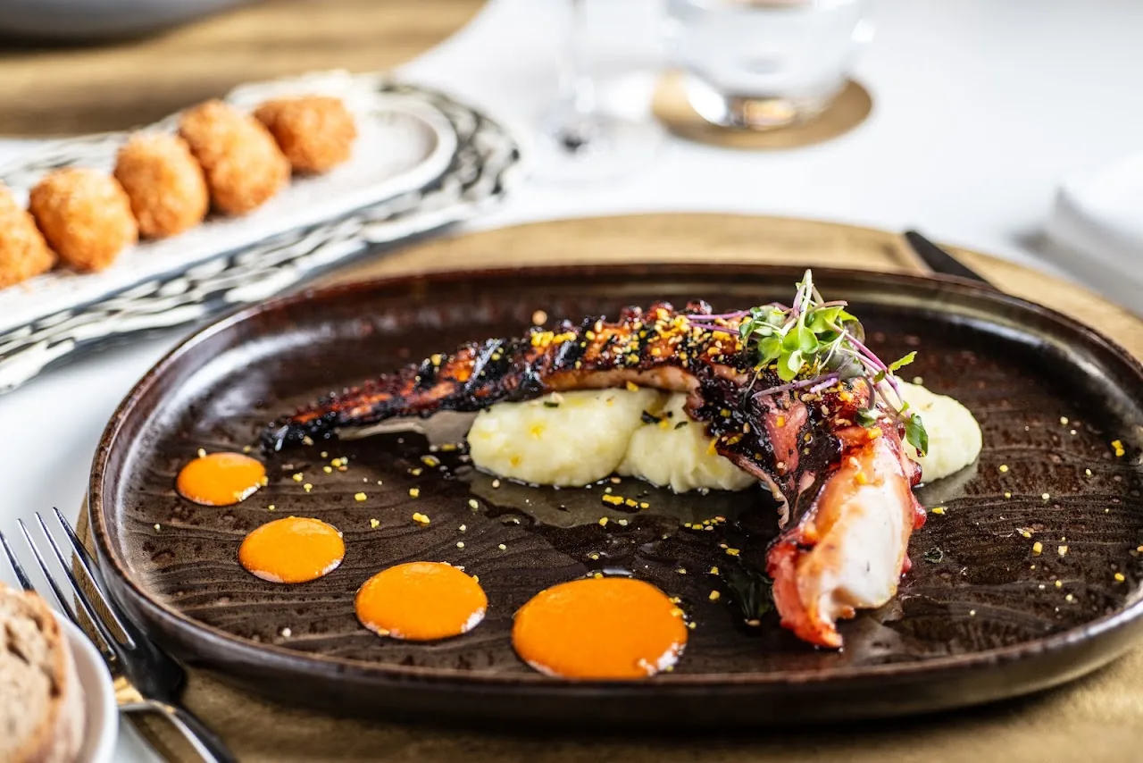 A plate of grilled octopus with dots of orange sauce and mashed potato