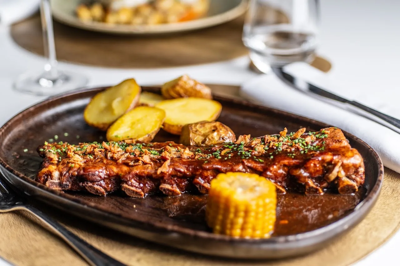 A rack of ribs with roasted potatoes and a piece of corn on the cob