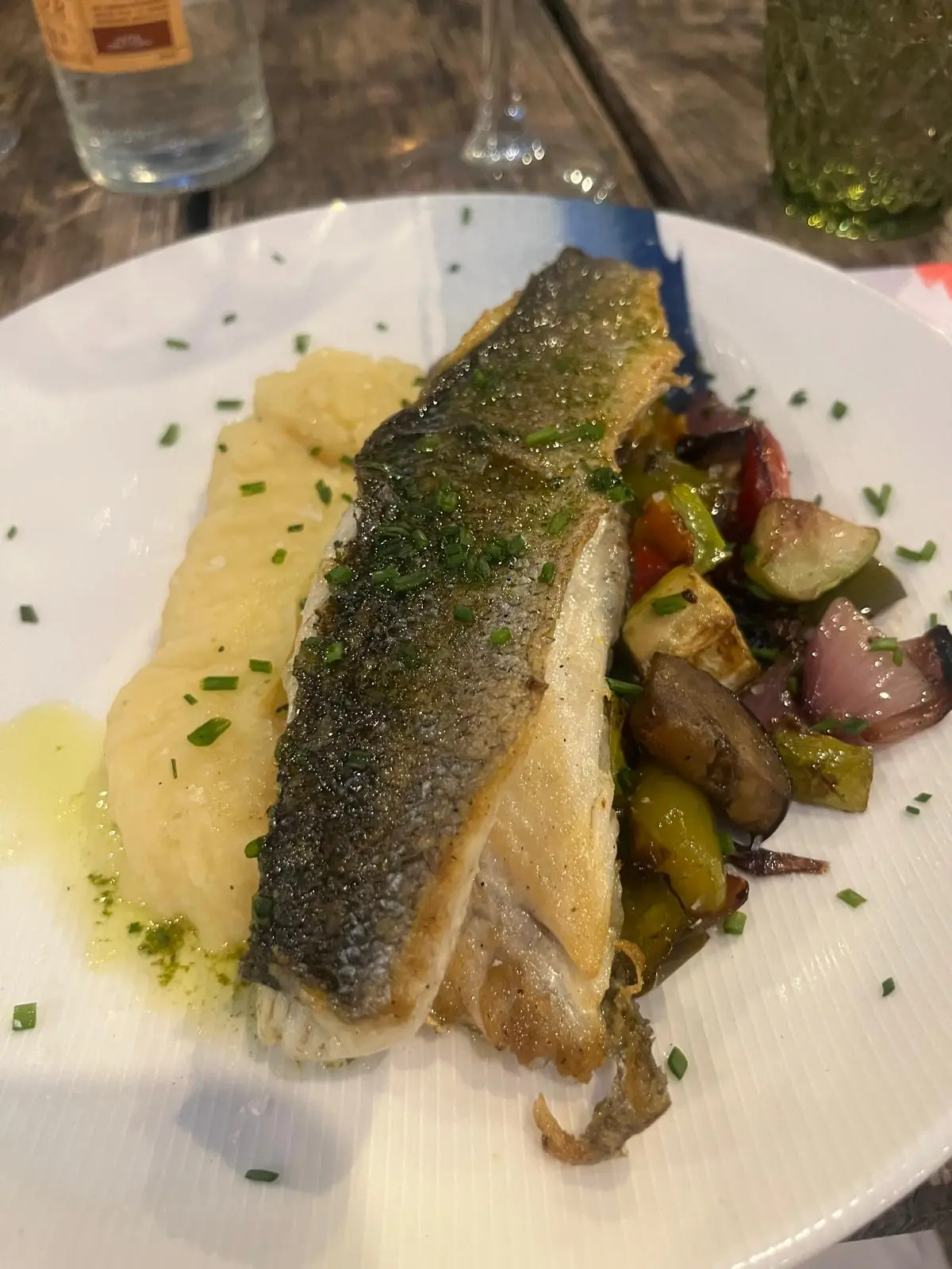 A grilled fish fillet with roasted vegetables and potatoes.
