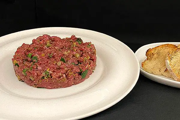 Beef tartare on a round white plate with toasted bread slices