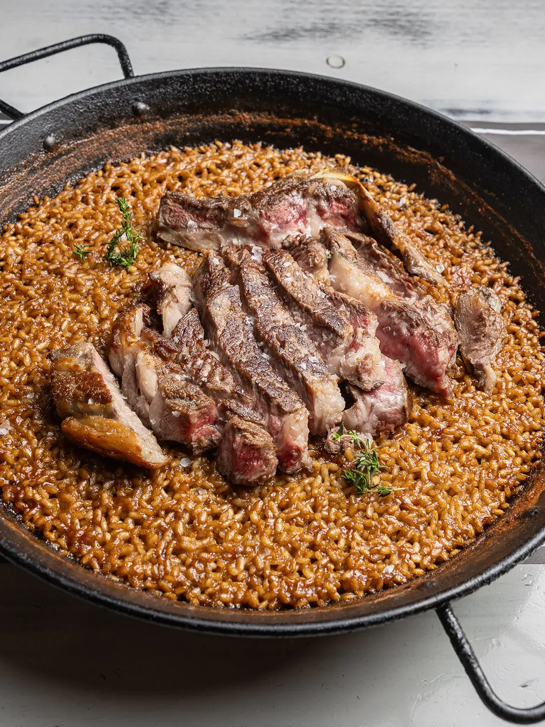 Seared sliced steak fanned over saffron rice in a paella pan, garnished with thyme sprigs, at Restaurant La Pepa