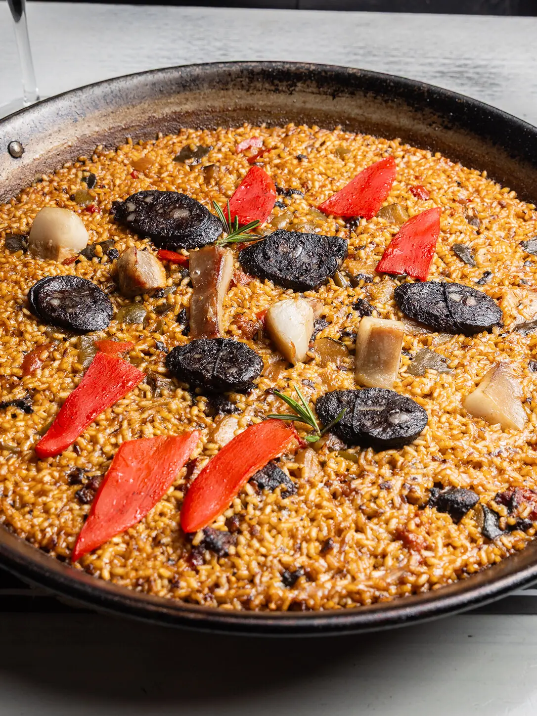 Paella-style rice topped with slices of black pudding, roasted red pepper strips, and scallops, garnished with rosemary, at Restaurant La Pepa