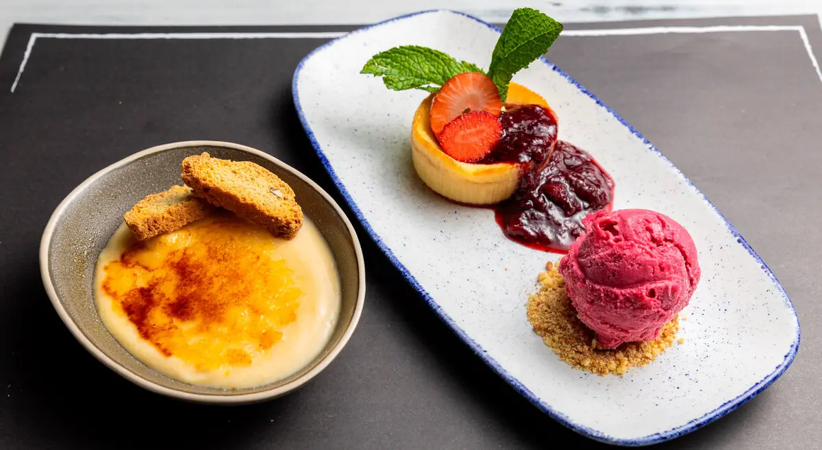 A creme brulee with biscuits alongside a small cheesecake, berry compote, and a scoop of pink sorbet on a plate, at Restaurant La Pepa