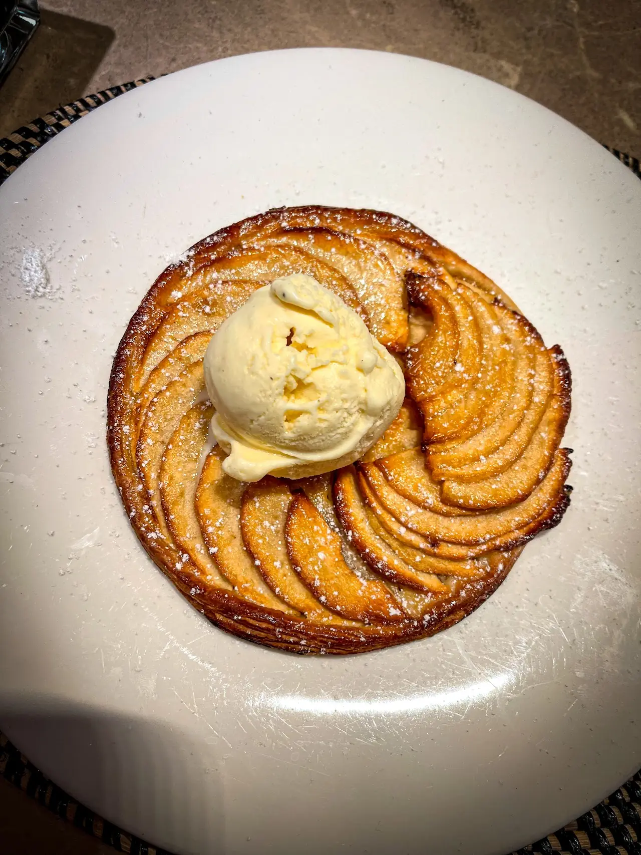 Thin apple tart with a scoop of ice cream, dusted with powdered sugar