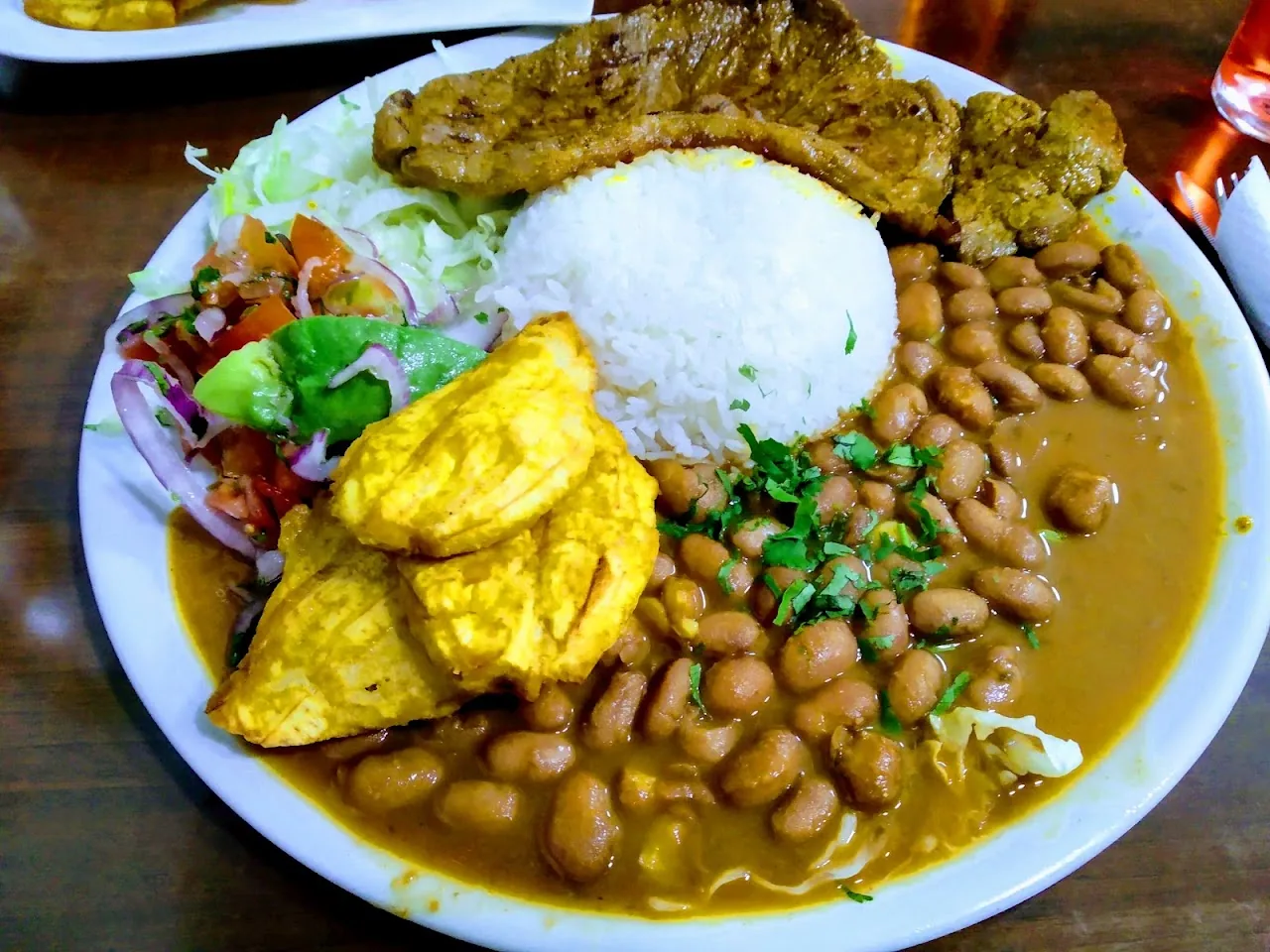A plate of rice, beans, fried plantain, meat, and salad, Ecuadorian-style combo plate