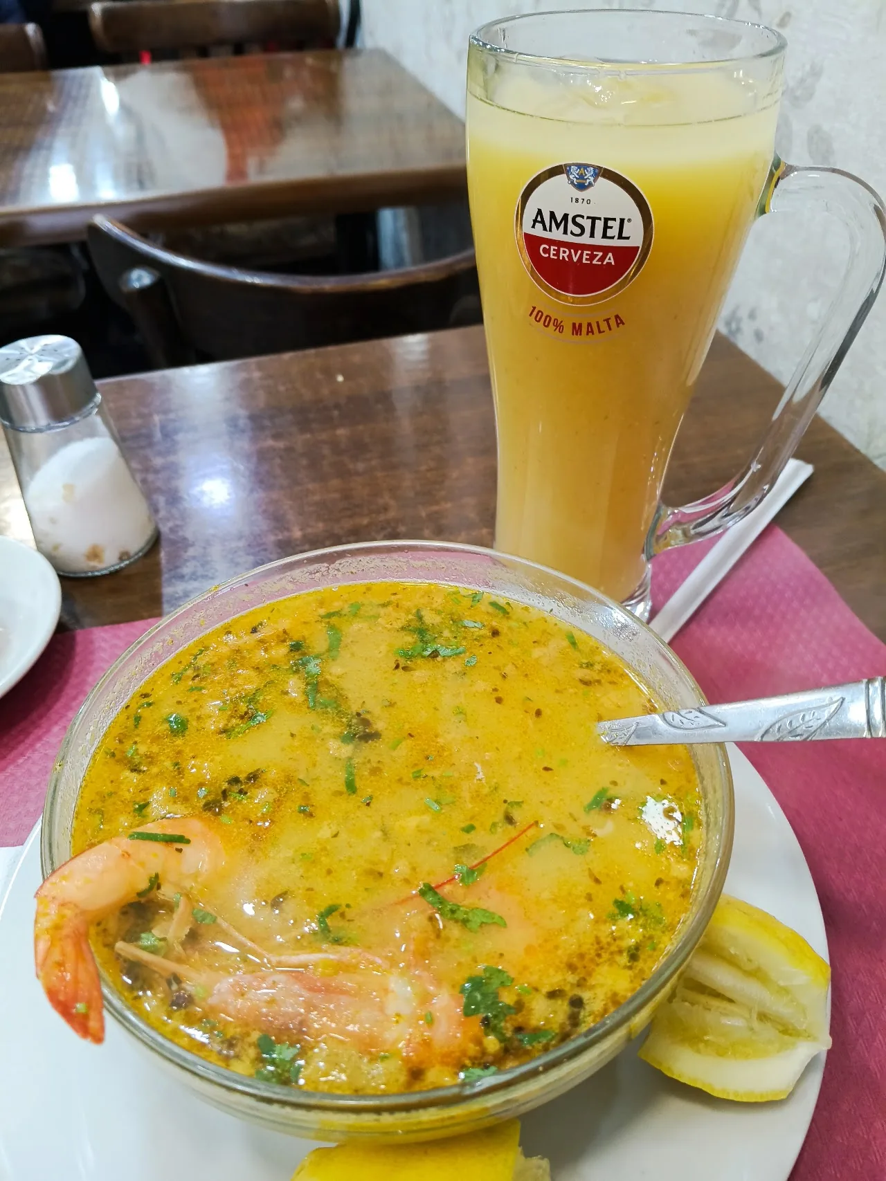 A bowl of seafood soup with shrimp, served with a glass of beer