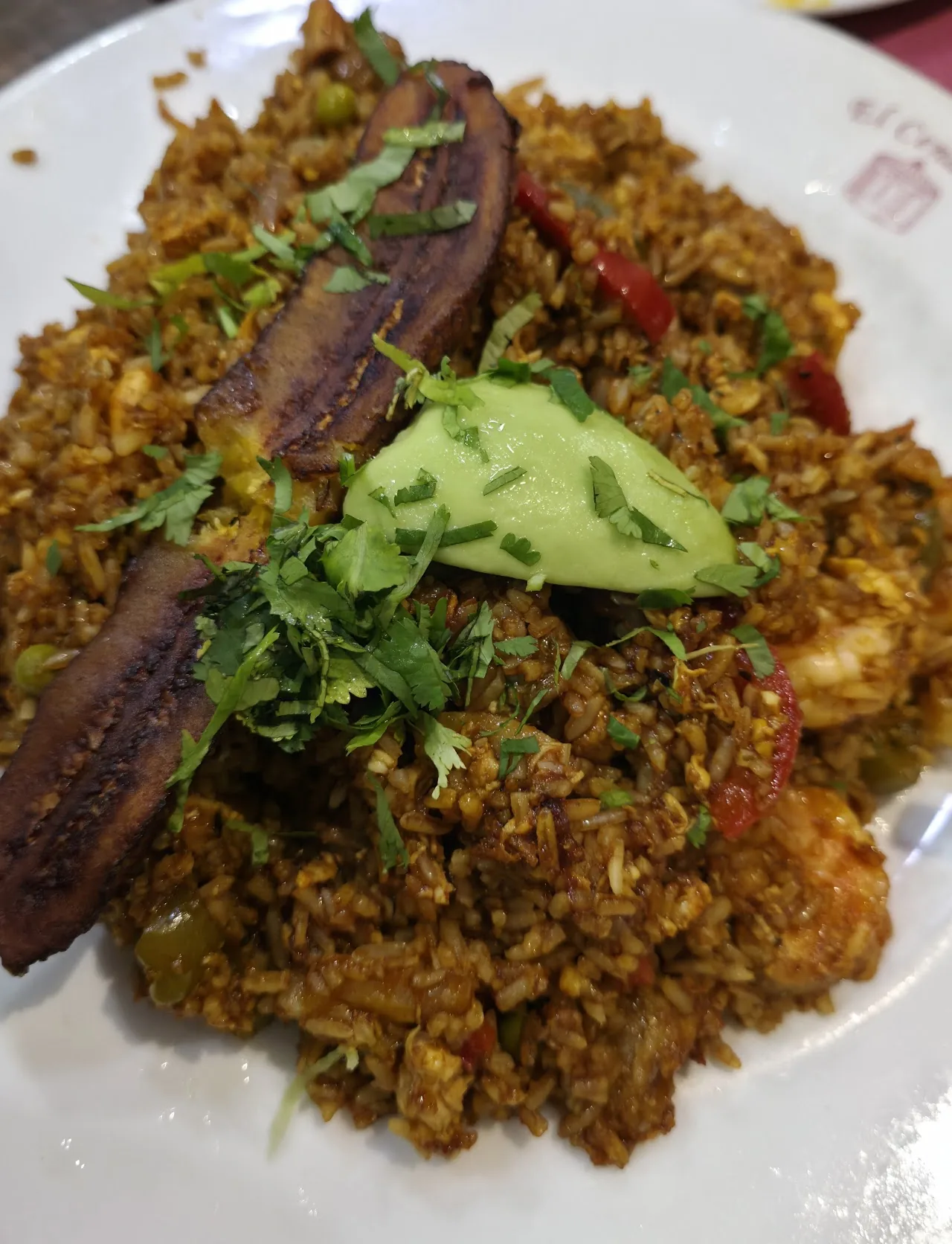 A plate of seasoned rice with fried plantain and sliced avocado