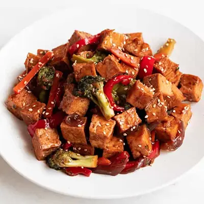 Bowl of glazed tofu cubes stir-fried with broccoli and red pepper, sprinkled with sesame seeds