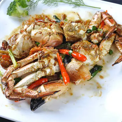 Stir-fried crab pieces with red chillies, spring onion and herbs on a white plate