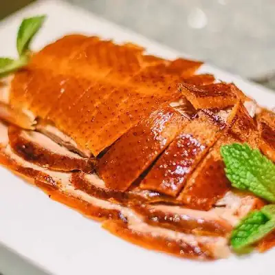 Sliced lacquered Peking-style roast duck with crisp skin arranged on a white platter with mint leaves