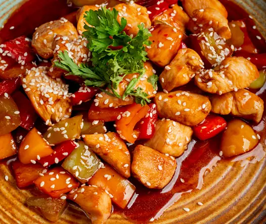 Sweet-and-sour chicken with peppers and pineapple in glossy red sauce, topped with sesame and parsley
