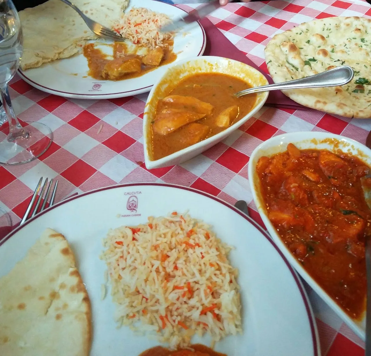 Three plates of Indian curry and rice served with naan bread