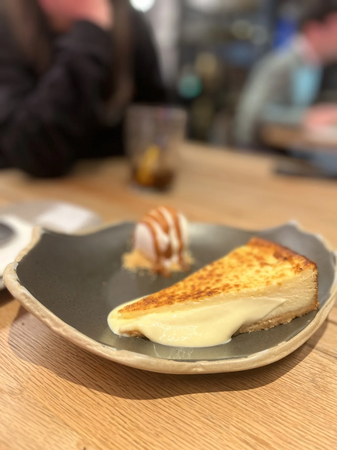 A slice of cheesecake on a dark plate with caramel drizzle