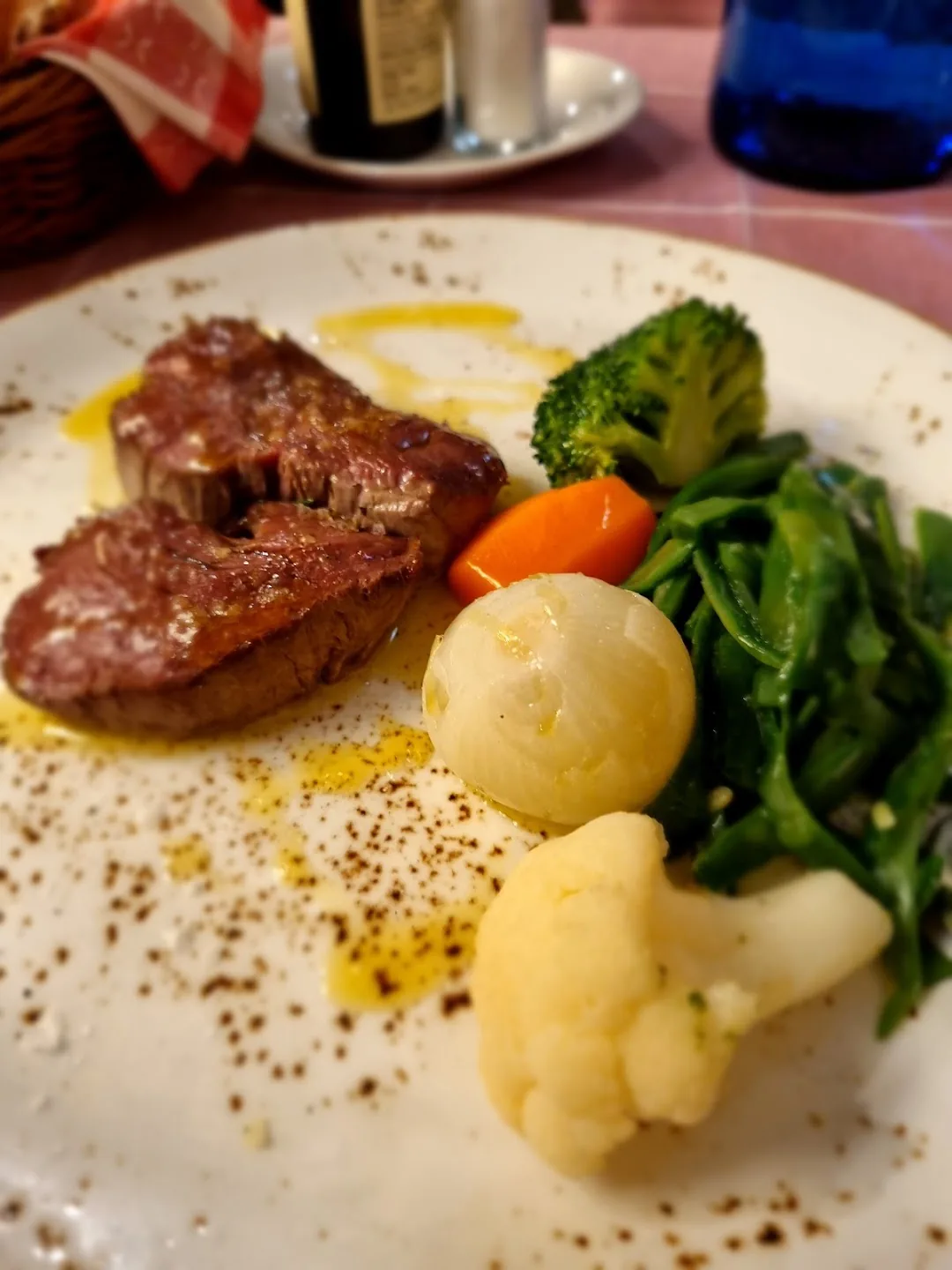 Sliced seared beef with steamed broccoli, carrot, pearl onion, cauliflower, and green beans on a white plate