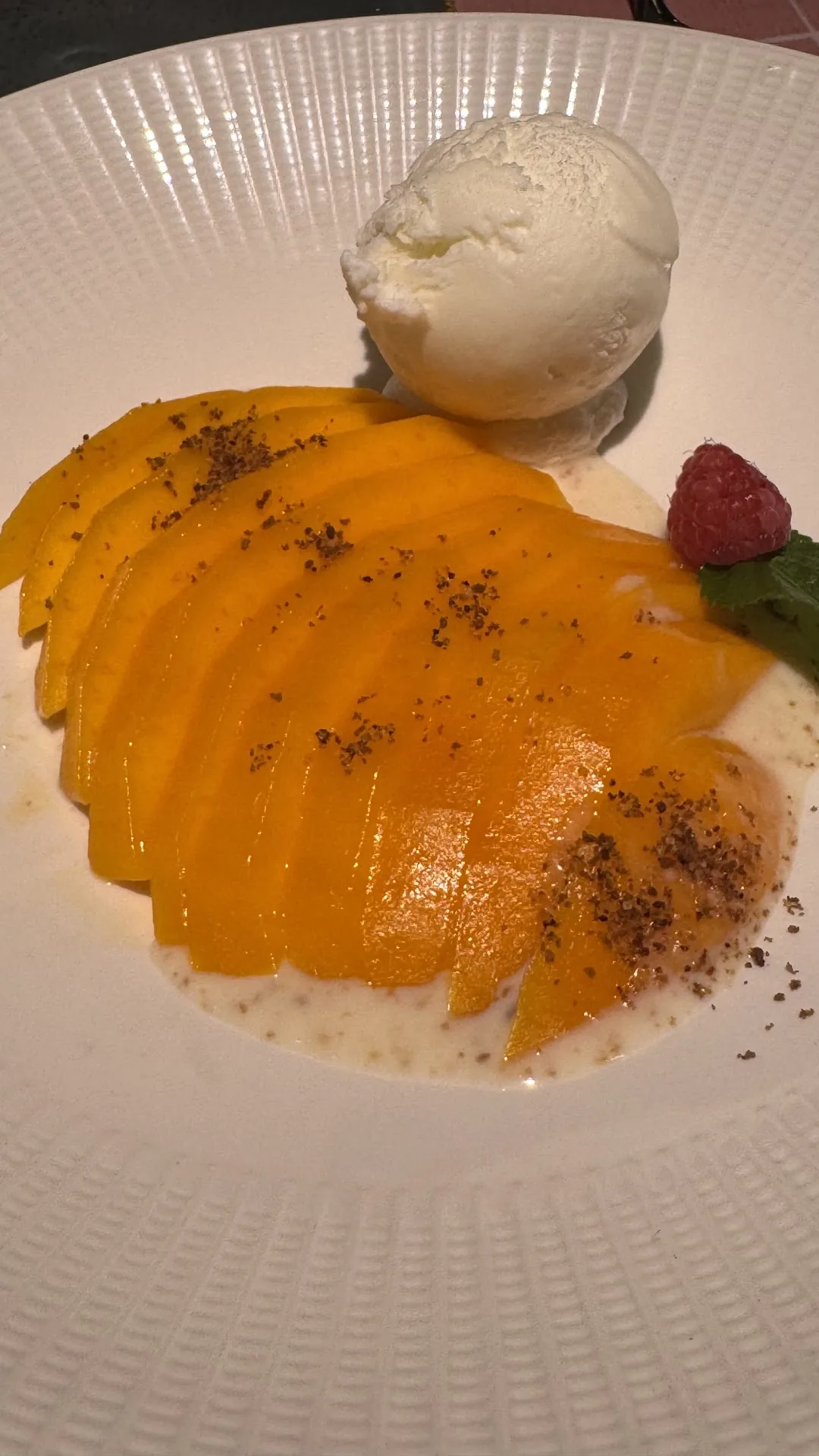 Fanned mango slices dusted with spice beside a scoop of ice cream and a raspberry garnish