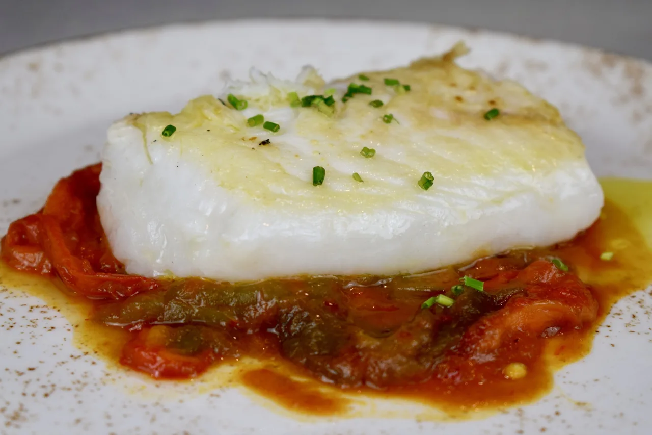 A thick white fish fillet on a bed of tomato and pepper sauce