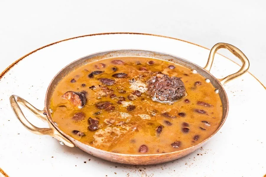 A copper pan of beans with a dark sausage in an orange sauce