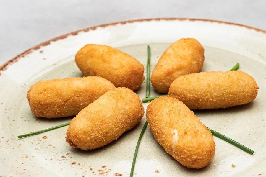 Five golden croquettes arranged on a plate with chives