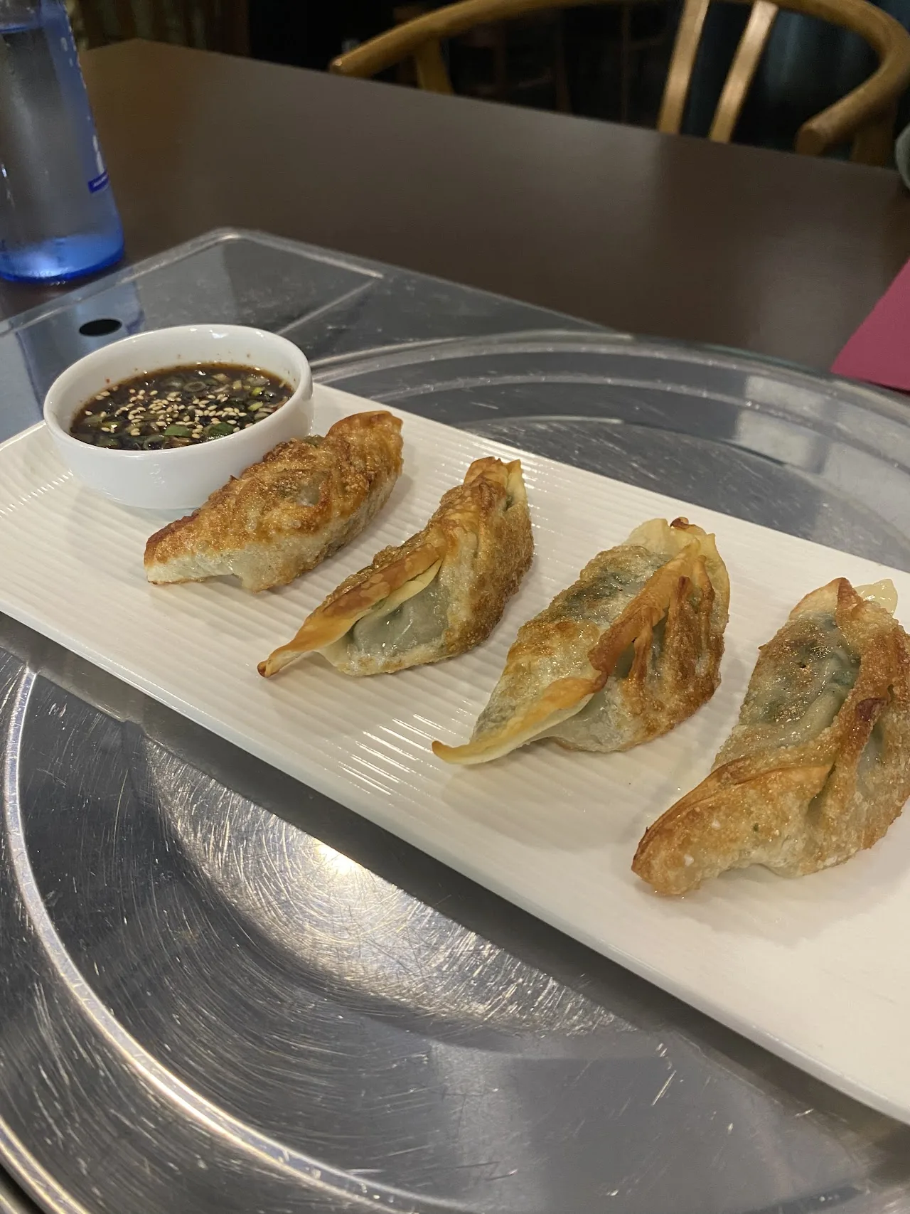 Five pan-fried dumplings on a white plate with dipping sauce