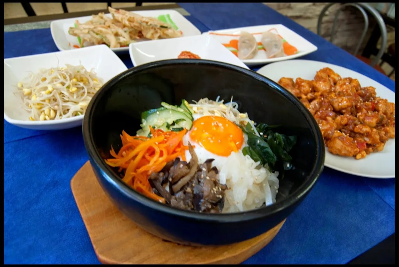A stone bowl of bibimbap with a fried egg and vegetables, served with side dishes