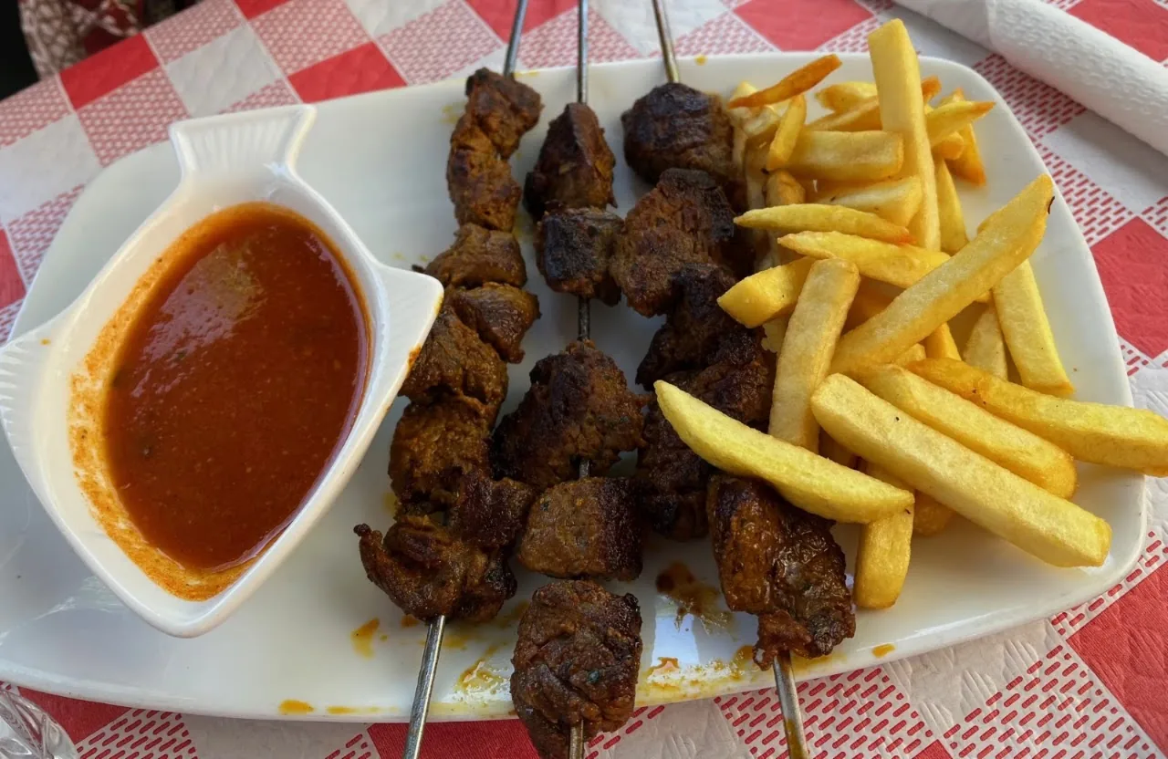 Grilled meat skewers with a side of fries and a red dipping sauce